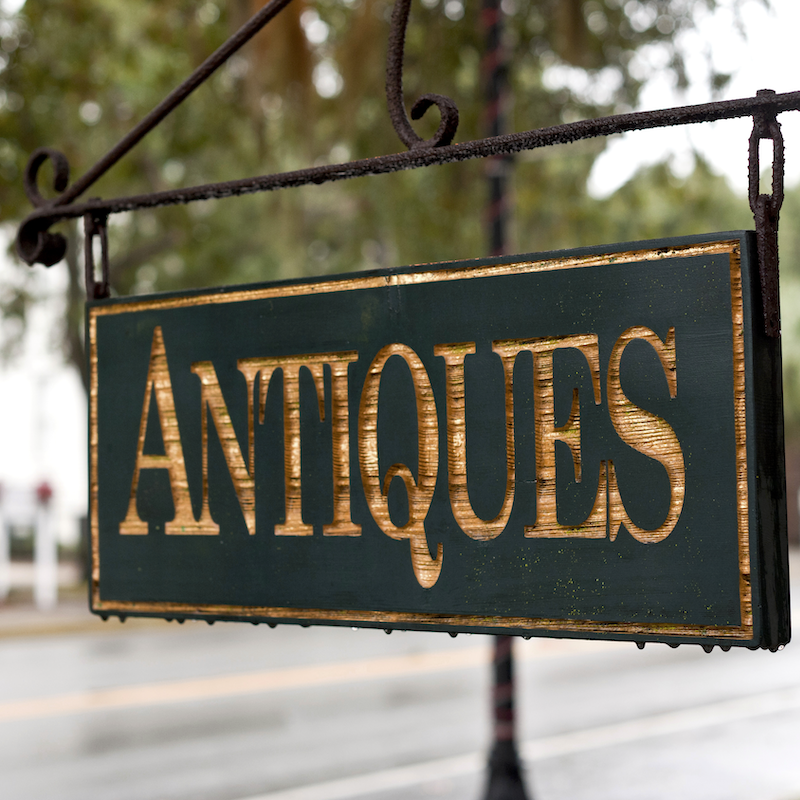 A green and gold Antiques store sign hangs outside a building.